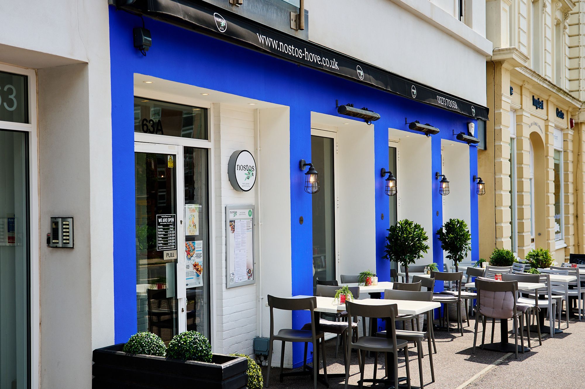 Nostos Hove - exterior shot of the venue, blue walls and chairs and tables in front of the venue