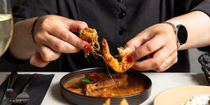 person holding shrimp above the shrimp dish served in the black table at Nostos hove