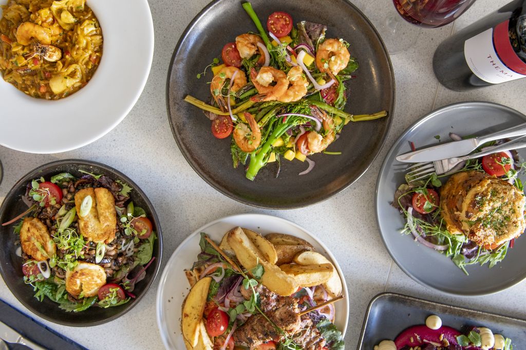 A variety of main dishes served on ceramic plates and bowls. Including a prawn salad with broccoli.