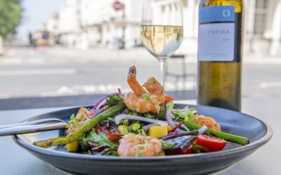 A black dish of large prawns with seasonal roasted vegetables and a bottle of white wine.