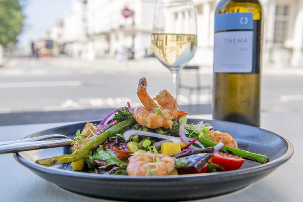 A black dish of large prawns with seasonal roasted vegetables and a bottle of white wine.