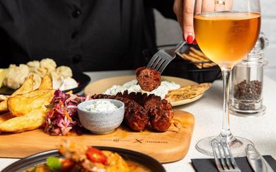 Person cutting meat sausage served on board with white sauce