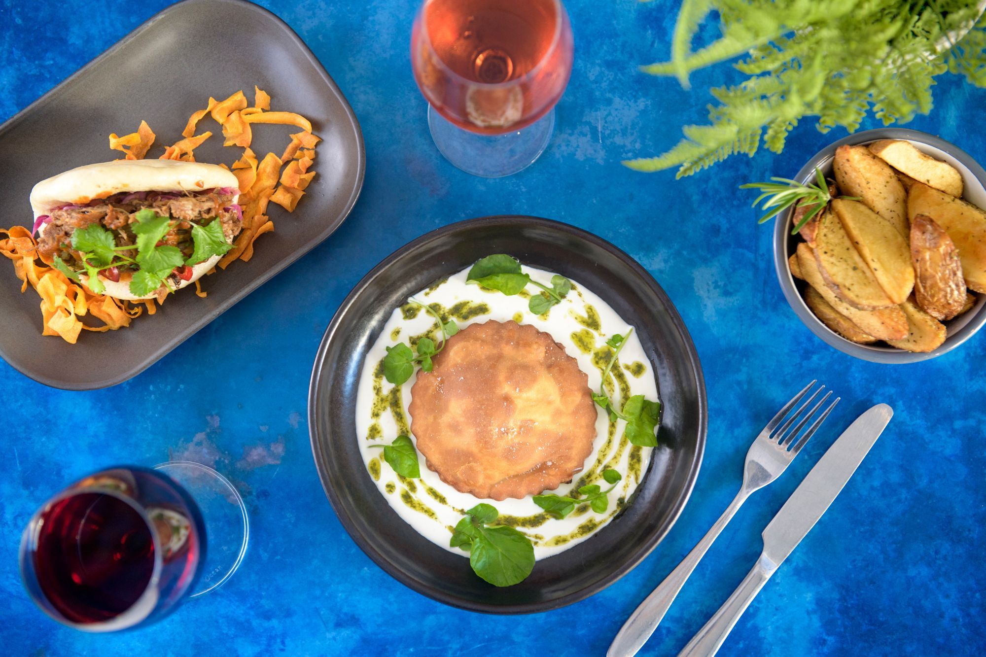 over head shot of the couple of greek dishes served on black plates with glasses of red wine - Nostos restaurant in Hove