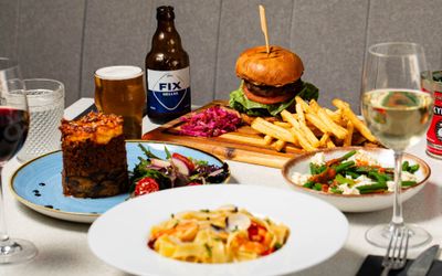 side shot of the table laid out with few dishes inlsuding burger and chips, pasta, drinks