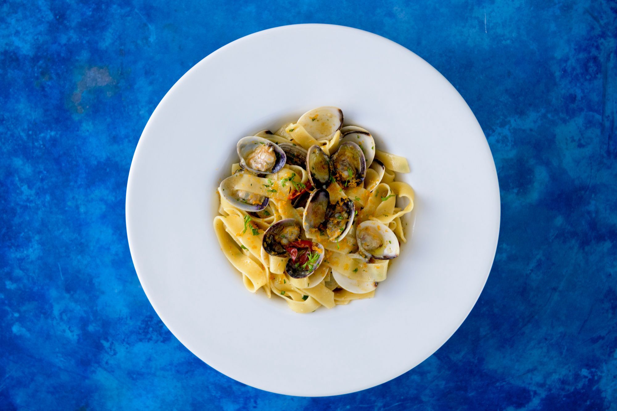 over head shot of the white plate with pasta and seafood one the dark blue table