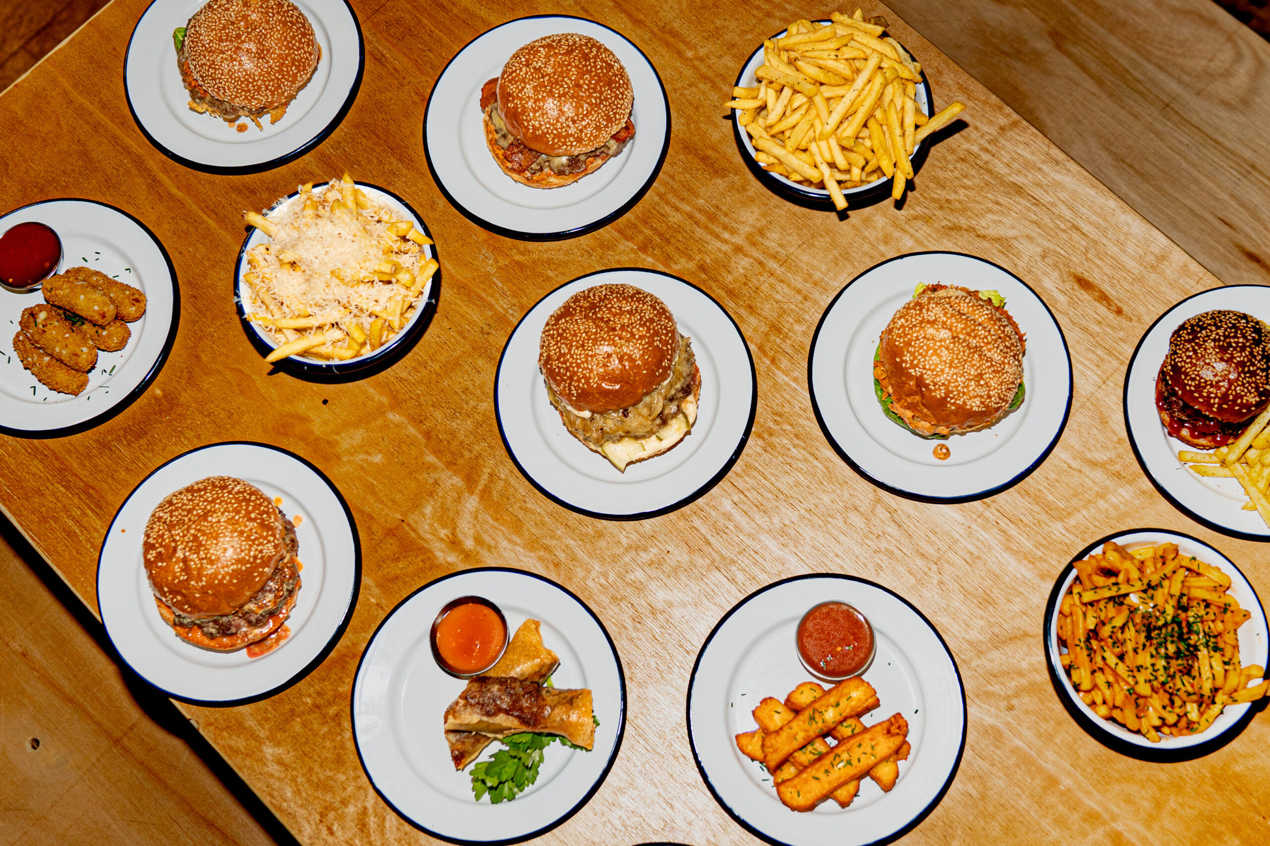 over head shot of the light brown wooden table laid out with bowls of chips and multiple burgers