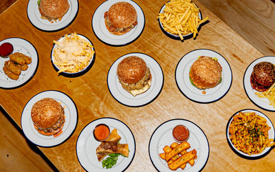 over head shot of the light brown wooden table laid out with bowls of chips and multiple burgers