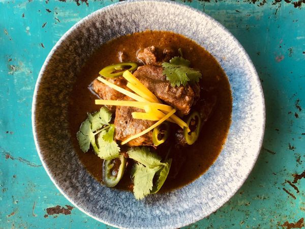 Slow cooked beef shin served in a deep light grey bowl garnished with coriander and green chilli 