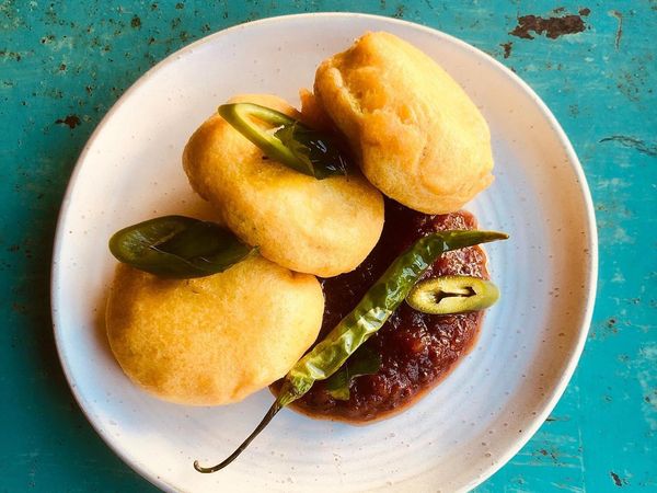 Spiced mashed potatoe balls with salted and fried chilli and garlic and tomato chutney, on a round white and grey speckled plate and a turquoise table