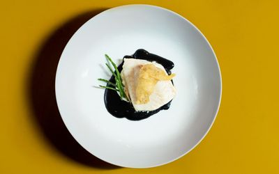 Brill with squid ink velouté , oyster tempura and samphire. Photographed on a mustard yellow table.