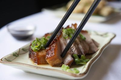 Sliced pork garnished with spring onions being eaten with chopsticks.