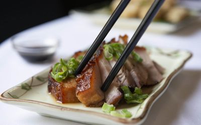 Sliced pork and chopsticks. Sliced pork garnished with spring onions being eaten with chopsticks.