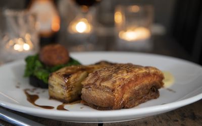 A candlelit Sunday lunch of roast pork with crackling served with a drizzle of gravy and greens.