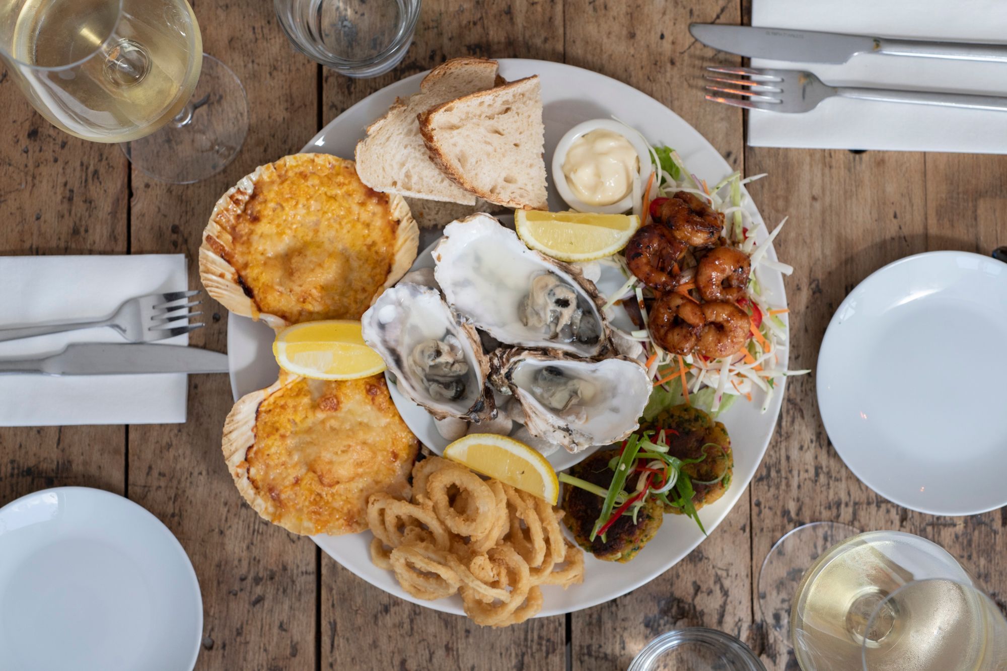 table laid out with big plate with 3 Irish rock oysters on, onion rings, slice bread and white wine on the side. Morleys Bistro Hurstpierpoint, seafood platter