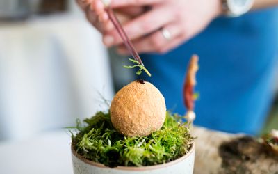A bowl of salad with an arancini ball being dressed for serving