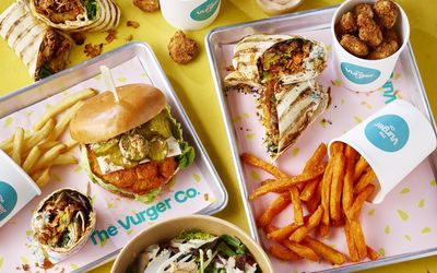 A spread of vegan fast food, burgers, wraps, chips and salad bowls.