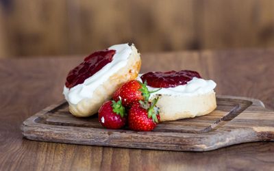 Cream tea scone with clotted cream and strawberry jam presented on a wooden chopping board with fresh strawberries.