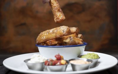 A metal bowl of chunky chips seasoned with sea salt served with a variety of dips in small pots.