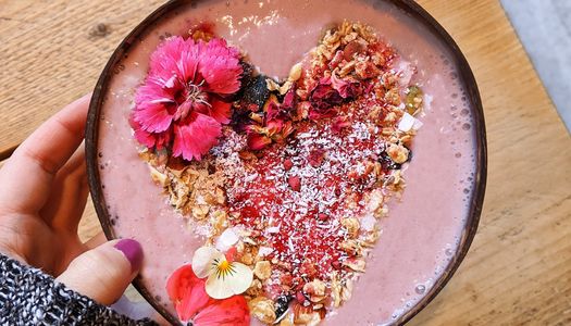 Pink breakfast bowl with a heart shaped granola topping and edible flowers.