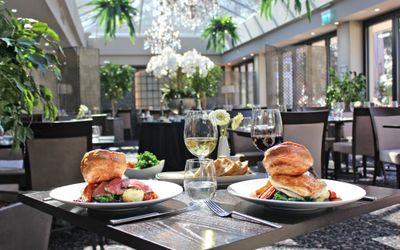 Interiors shot of dining tables in the bright restaurant with two plates of Sunday roast lunches served. The Glass House is a Health club with a Sussex restaurant for members and non members.