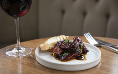A small plate of sticky ribs served with a glass of red wine.