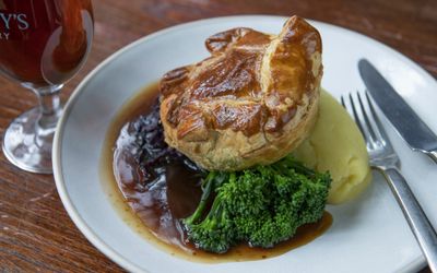 A close up photograph of a Sunday lunch made with a puff pastry pie, mash, red cabbage and Tenderstem broccoli