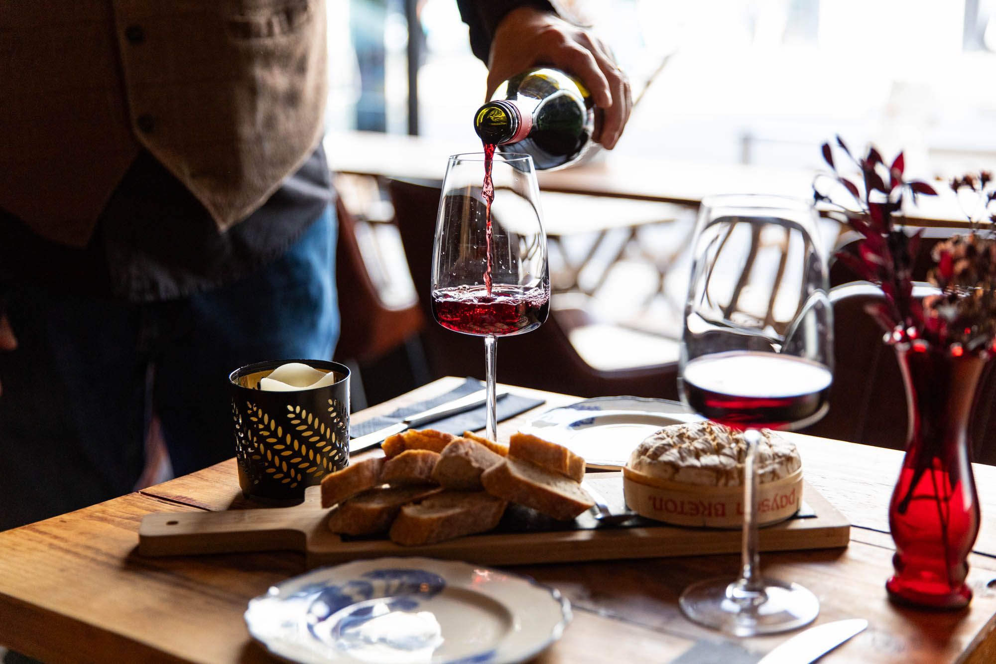 bartender pouring red wine into wine glass on the table with cheese and bread