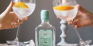 Toasting with a gin & tonic garnished with fresh orange and Brighton Gin bottle in the centre.
