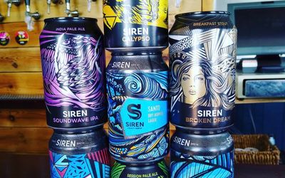 Colourful cans of craft beer stacked up with reflections on the bar top