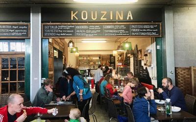 Hustle and bustle outside dining at Kouzina at the Brighton open market with people dining and the Kouzina sign displayed against the black paintwork. Greek Restaurant Brighton