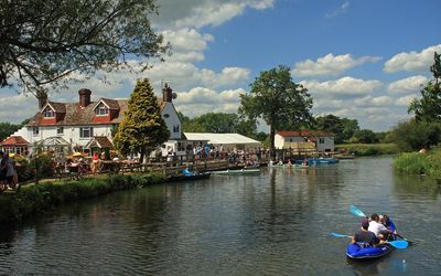 Landscape photo of The Anchor Inn next to the river with people kayaking in the water.