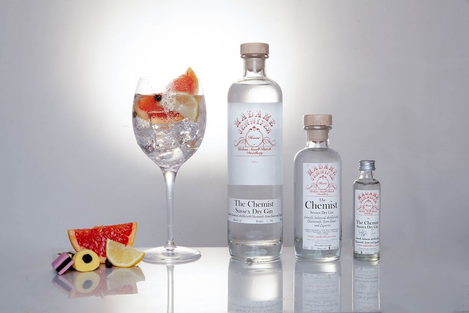 Three different sized bottles of Madame Jennifer gin and a large gin goblet with pink grapefruit garnish