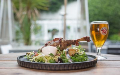 A plate of chicken and egg salad with a pint of beer on a wooden table in a pub garden.