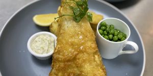 Battered fish with thick cut chips, peas and tartar sauce.