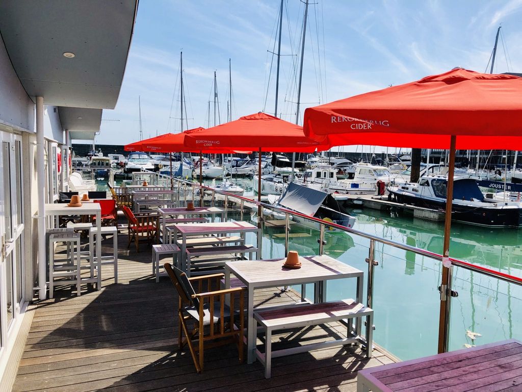 Water side decking and seating at The Watershed with red parasols for shade and views over the yachts