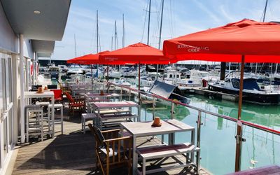 Water side decking and seating at The Watershed with red parasols for shade and views over the yachts. Brighton seafront restaurants guide. Brighton Seafront Bars. Brighton Marina Restaurants