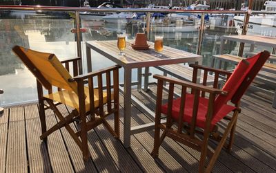 Two canvas chairs at a table on the Brighton marina waterfront with two beers on the table.