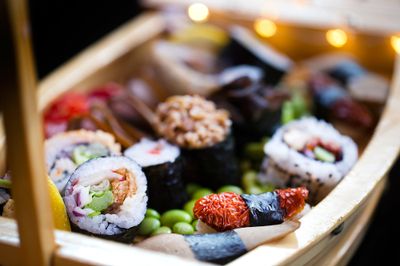 A wooden model ship displaying a selection of colourful sushi rolls on a bed of edamame beans.