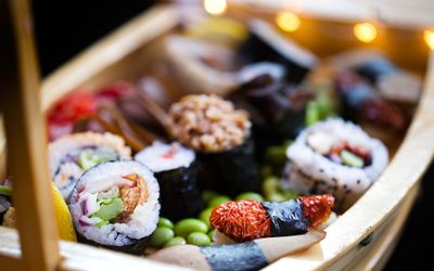 A wooden model ship displaying a selection of colourful sushi rolls on a bed of edamame beans.