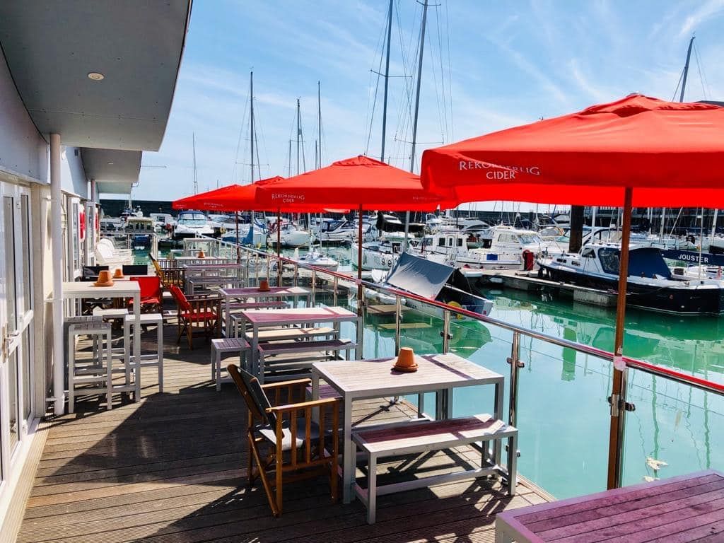 A row of tables with red parasols facing out on the Brighton marina front