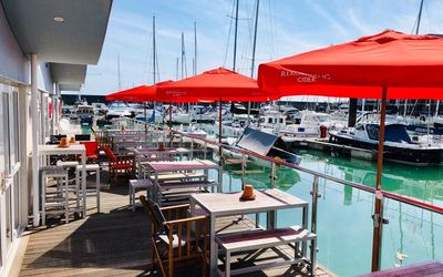 A row of tables with red parasols facing out on the Brighton marina front. Brighton Marina restaurants. Place to eat in Brighton marina. Brighton seafront restaurants
