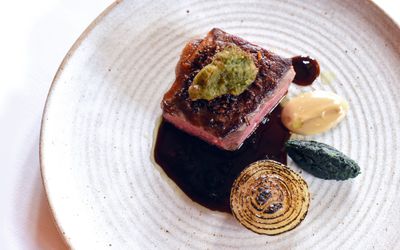 A stone coloured plate with a pice of rare cooked meat, burnt onion, jus and four purees.