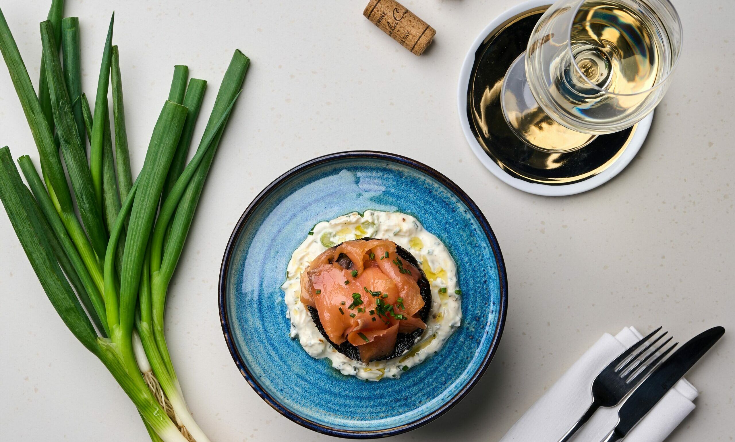 over head shot of the blue plate with salmon dish and glass of white wine and leek 