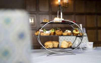 Three tiers of afternoon tea on a white tablecloth with dark wood wall paneling in the background. Cream tea at Mannings Heath.