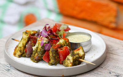 Paneer tikka skewers with a small metal pot of dipping sauce.