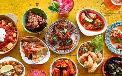 A colourful table full of plates and bowls of different tapas dishes served with cocktails.