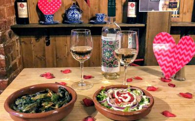 A valentine's table with two glasses of white wine and terracotta bowls of tapas food.
