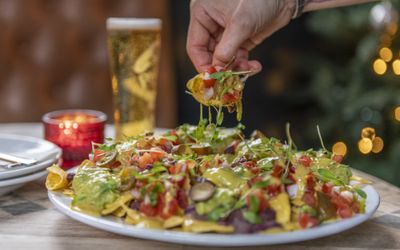 Cheesey Mexican nachos with guacamole and salsa served with a cold beer.
