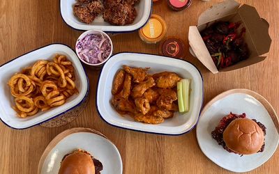 A selection of burgers, chicken wings, curly fries and dips photographed from above.