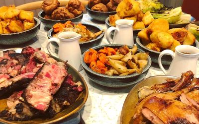 A roast dinner feast including bowls of roast potatoes, carrots, parsnips, jugs of gravy and sliced meats.